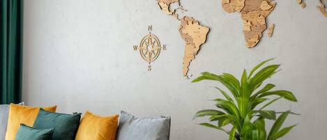 A world map wall decoration with a compass rose, a grey sofa with colorful cushions, and a green plant.