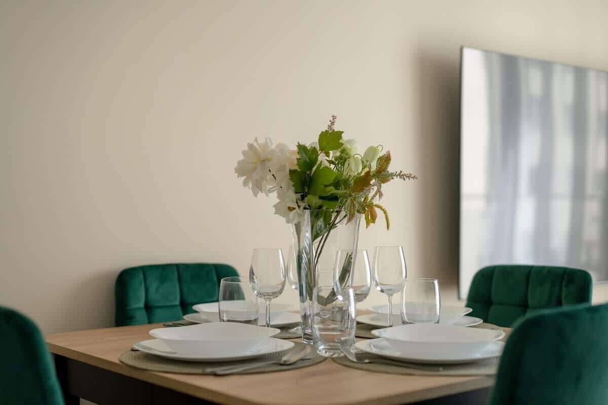 Een eettafel gedekt met witte borden, glazen en een vaas met witte bloemen.
