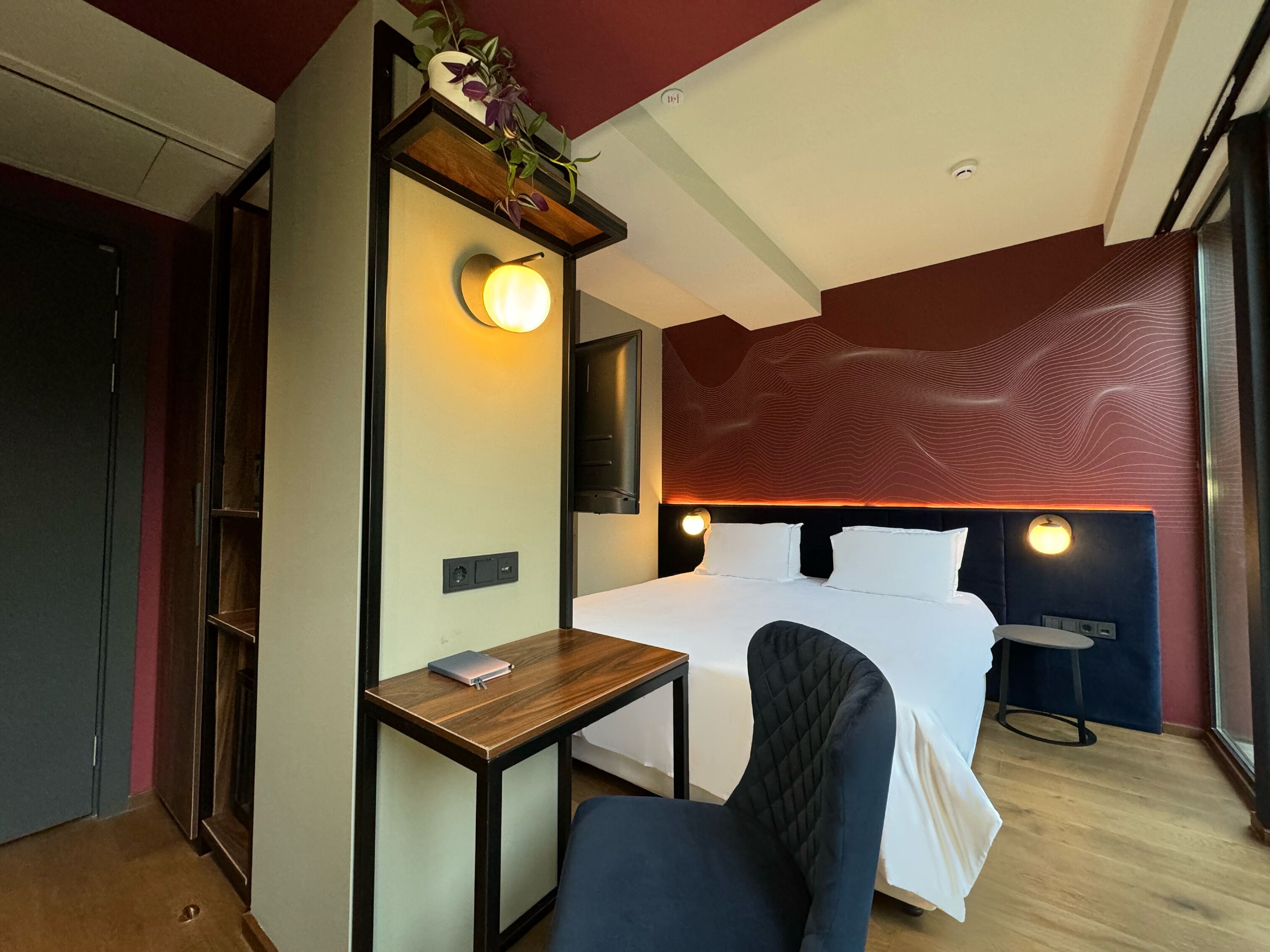 Una camera d'albergo con un letto, un comodino, una sedia e una TV fissata al muro.