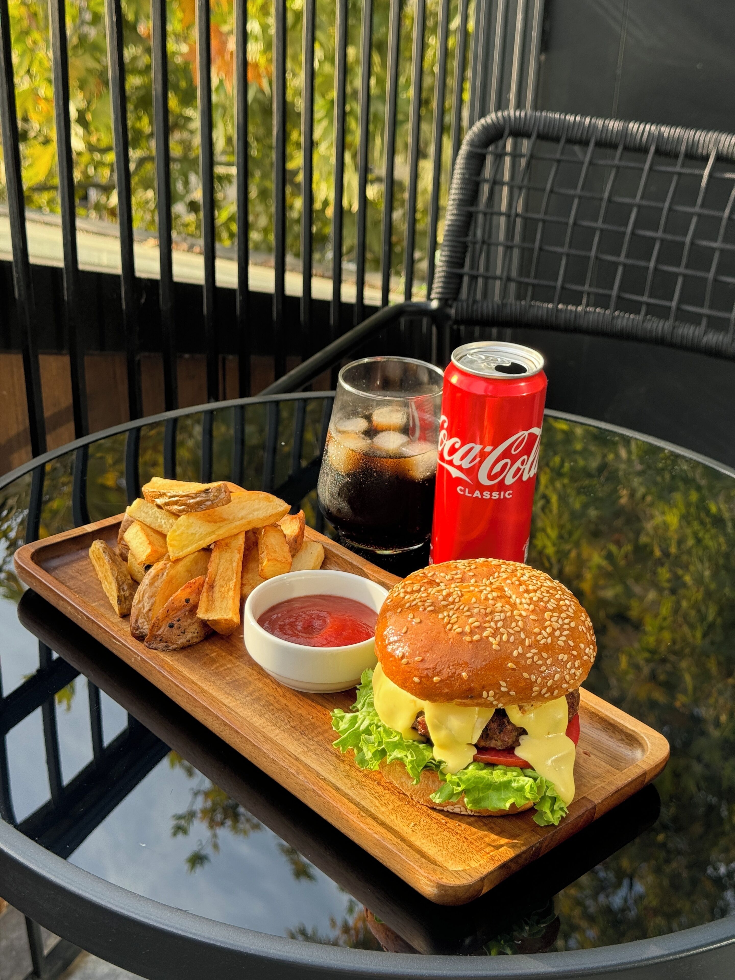 A tray with a burger, fries, ketchup, and a Coca-Cola can on a glass table.