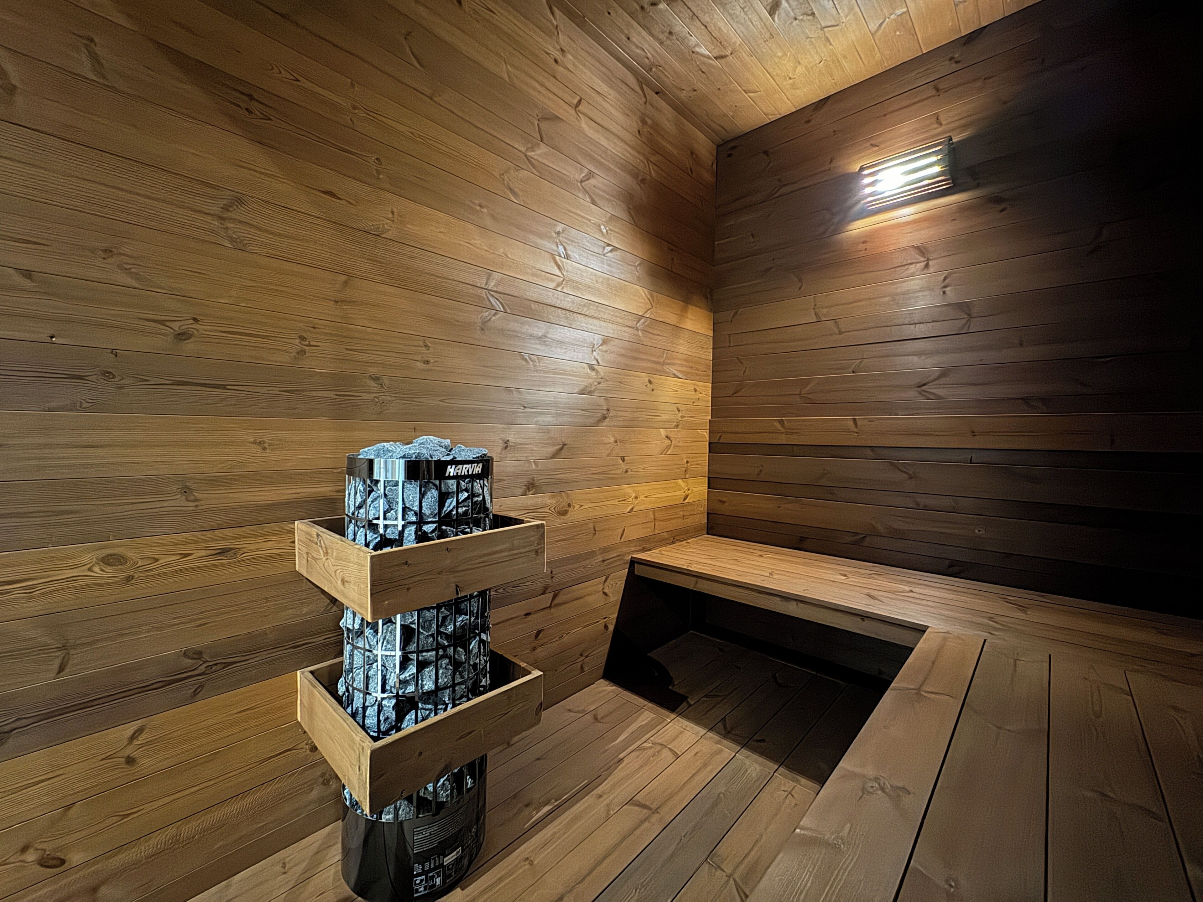 A sauna room with wooden walls and a bench. There is a wooden shelf with a black container holding towels.