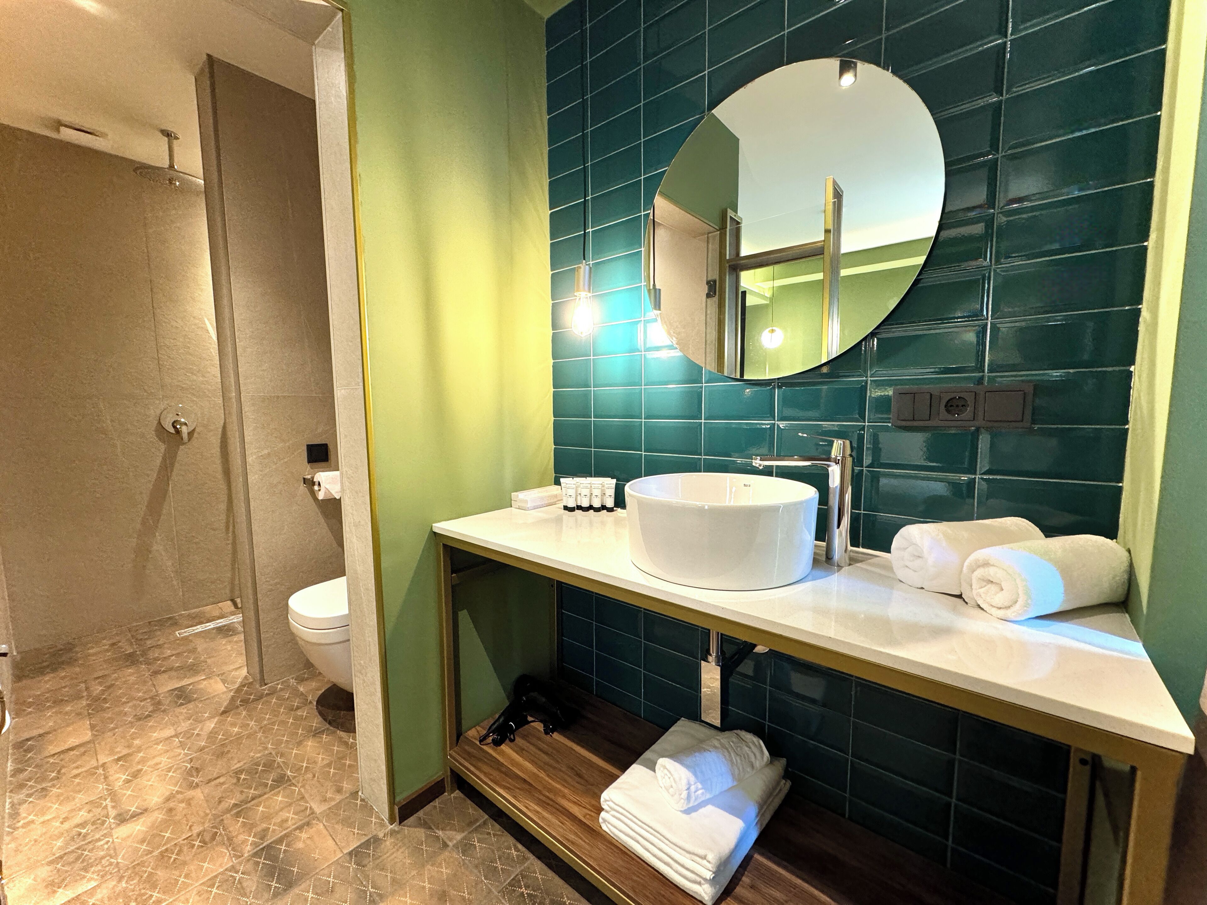 Une salle de bain moderne avec un lavabo blanc, un miroir rond et des carreaux verts.