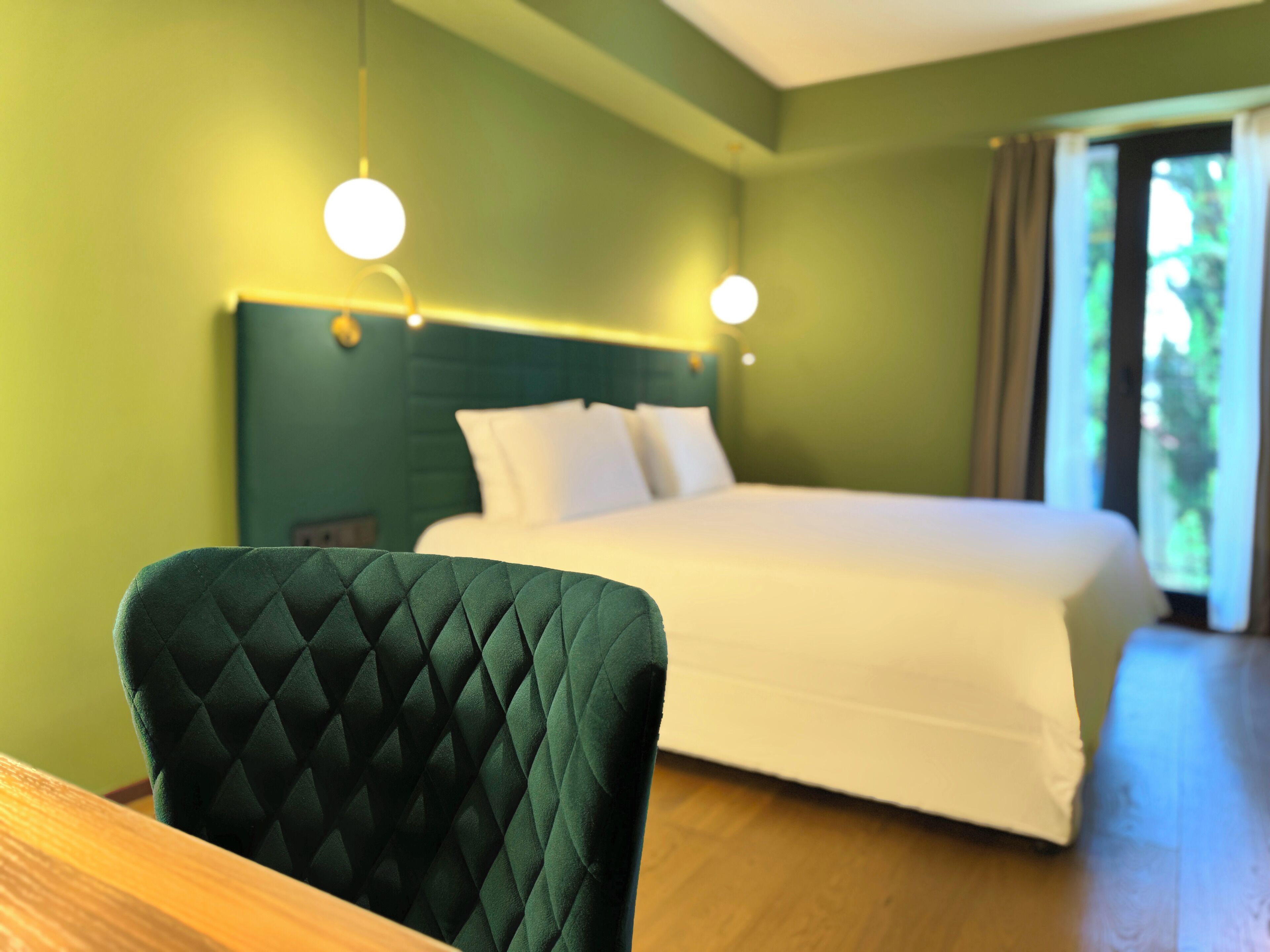 Una habitación de hotel con cama, un sillón tapizado en verde y dos lámparas de noche.