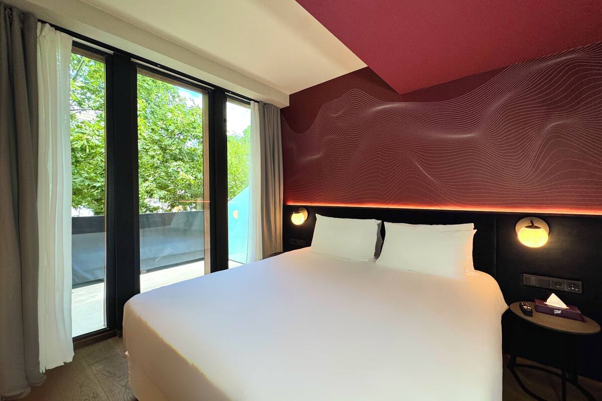 A hotel room with a large bed, a view of greenery outside, and a modern ceiling design.