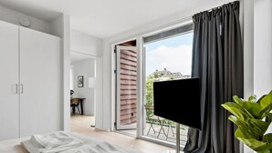 A bedroom with a bed, a TV, a plant, and a balcony with a view.