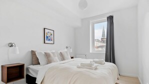 A bedroom with a bed, bedside tables, a window with curtains, a radiator, and a framed picture on the wall.