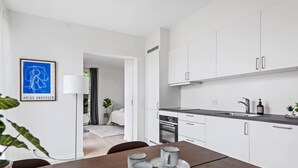 Una cocina moderna con armarios blancos, una mesa de comedor con algunas tazas y un cuadro en la pared.
