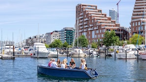 A boat with passengers docked at a marina with buildings in the background.