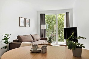 Una sala moderna con un sofá, una mesa de comedor con platos y tazas, una planta en maceta y un televisor.