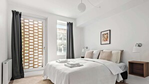 Un dormitorio con una cama, una ventana con cortinas, un cuadro en la pared y una mesita de noche.