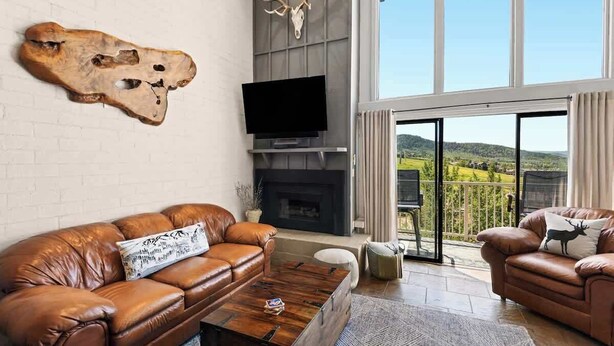 A living room with a leather sofa, a flat-screen TV, a fireplace, and a large window with a view of the countryside. - Vista Viewhaus Lodge (Steamboat Springs)