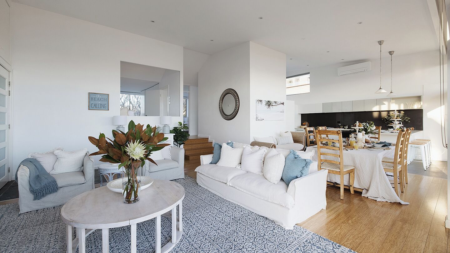 A spacious living room with a white sofa, a round coffee table, and a dining area with a table and chairs.