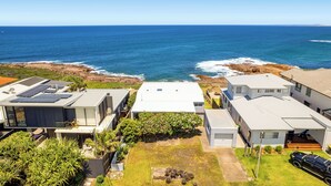 Un área residencial costera con casas modernas, un patio con césped y vista al océano.