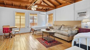 A room with a wooden ceiling, a bed, a sofa, a dining table with chairs, and a small table with a lamp. - Cozy Tiny Home for Couples Near Lafayette Hotspots (Lafayette)