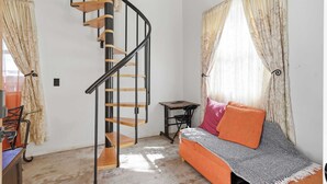 A compact living space with a spiral staircase, a sofa with cushions, a small table, and a chair. - Cozy Tiny Home for Couples Near Lafayette Hotspots (Lafayette)