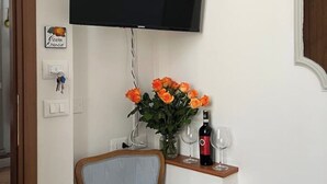 Et værelse med et fladskærms-TV monteret på væggen, en vase med orange blomster på et bord, og en flaske vin.
