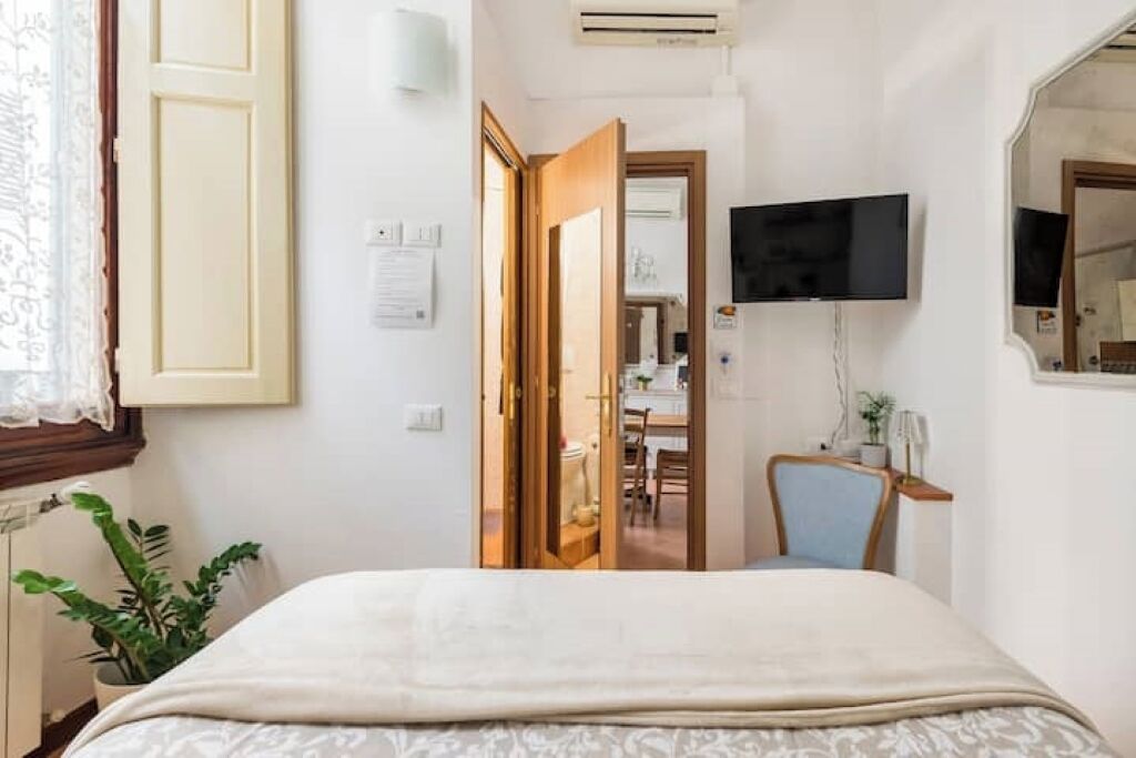 Een hotelkamer met een bed, een aan de muur bevestigde televisie, een bureau met stoel en een deur naar de badkamer.
