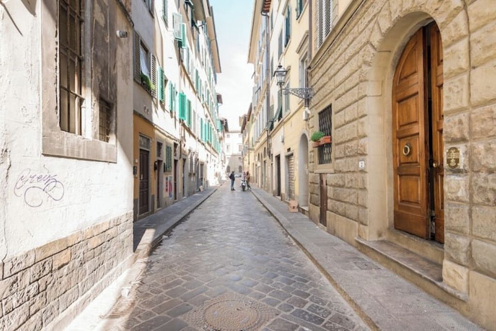 A narrow cobblestone street lined with historic buildings, featuring stone facades and wooden doors.