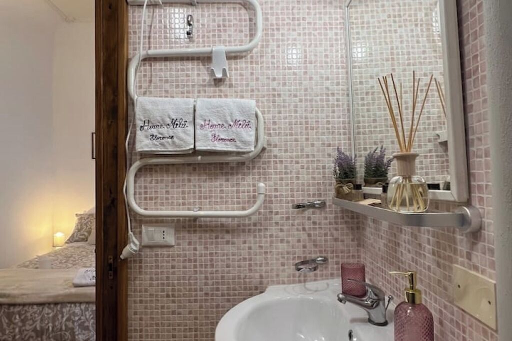 Un baño con una pared de azulejos rosa, un lavamanos blanco, un espejo y un perchero con dos toallas.