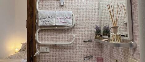 Un baño con una pared de azulejos rosa, un lavamanos blanco, un espejo y un perchero con dos toallas.