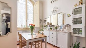 Spiseområde med et træbord og stole, et hvidt skab med glasdøre, og et vindue med udsigt.