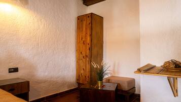 Una habitación acogedora con un armario de madera, una mesita con una planta, un banco y un estante con adornos.