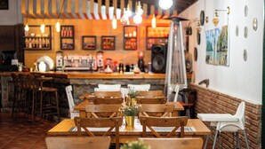 Ein Restaurantinneres mit Holztischen und -stühlen, hängenden Pendelleuchten und einer Ziegelwand.