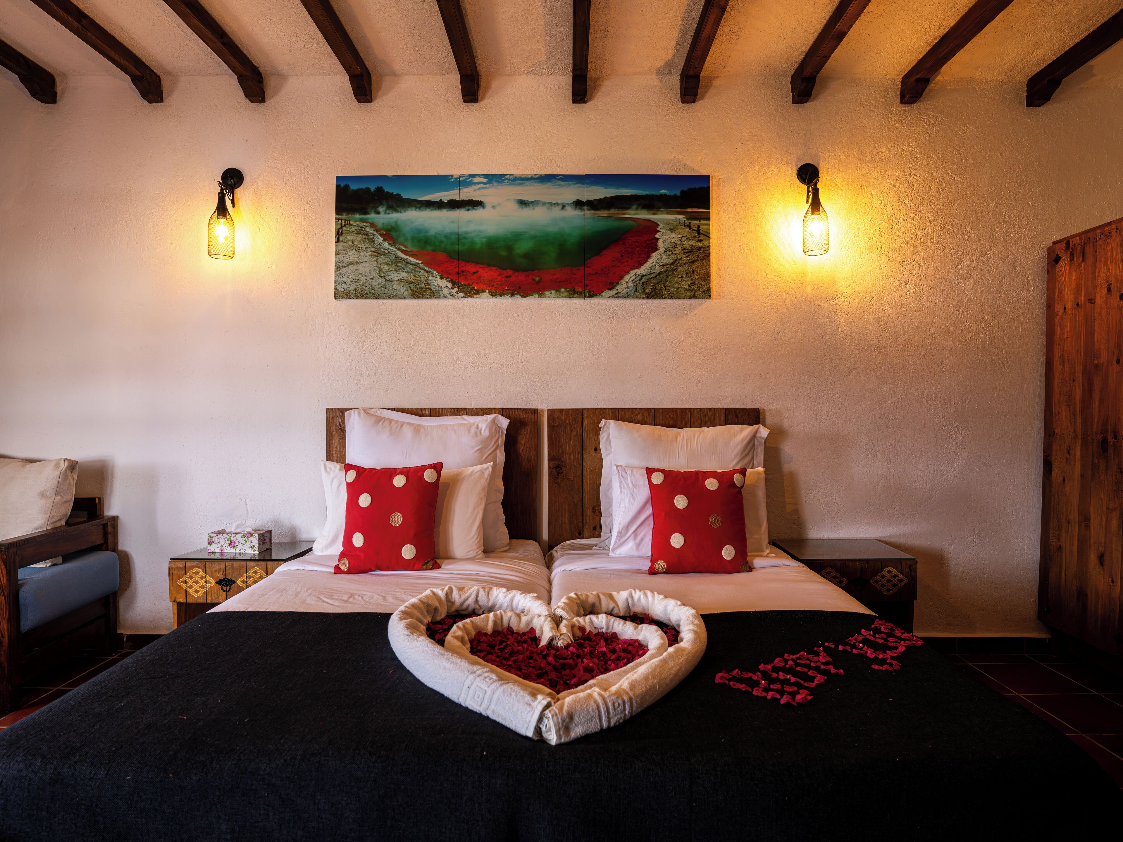 A hotel room with a wooden headboard, a painting of a landscape, and two wall-mounted lights.