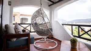 Ein Balkon mit Hängesessel, Holztisch und Blumentopf.