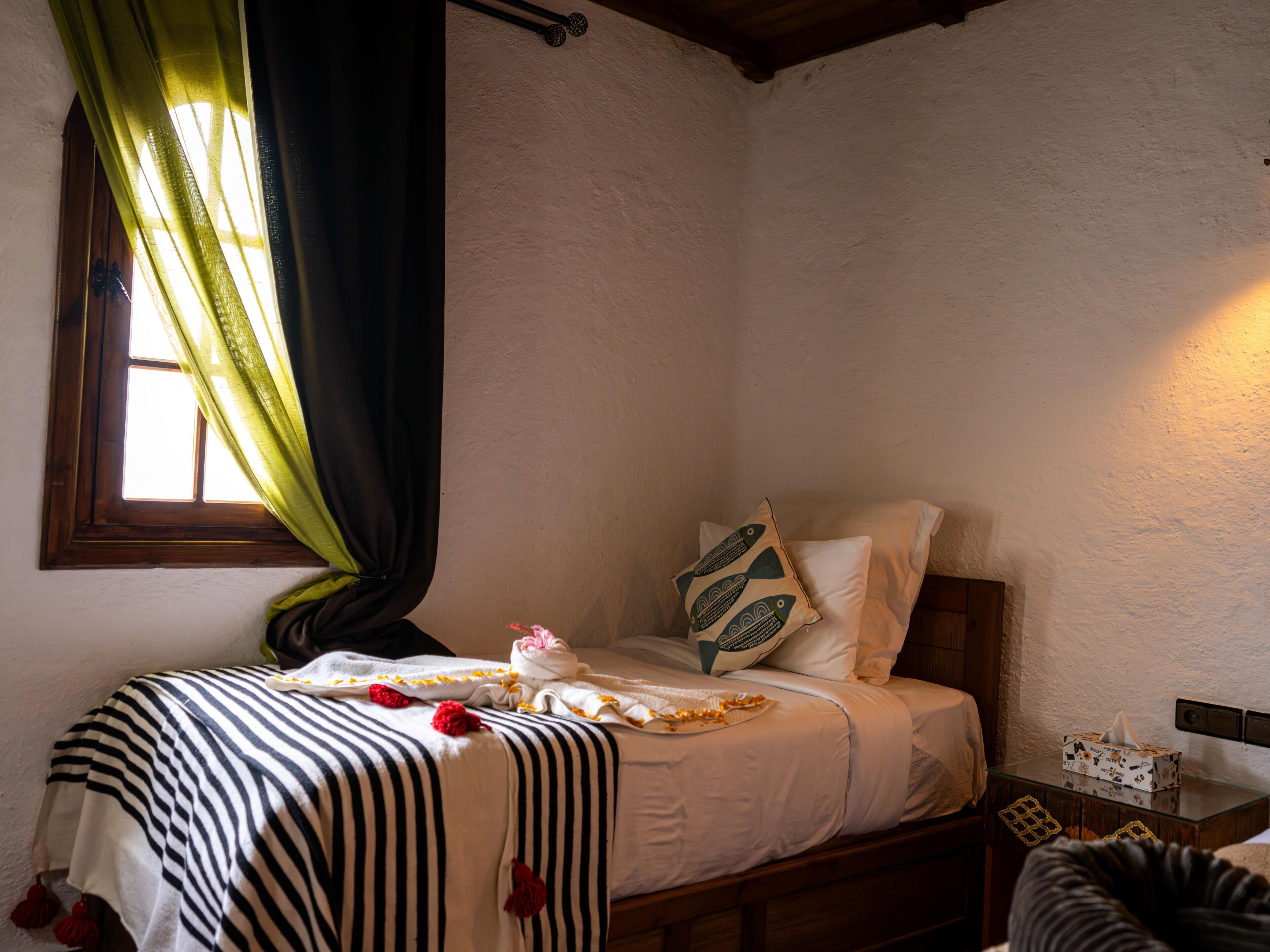 A bedroom with a bed, a window with curtains, a bedside table, and a lamp.