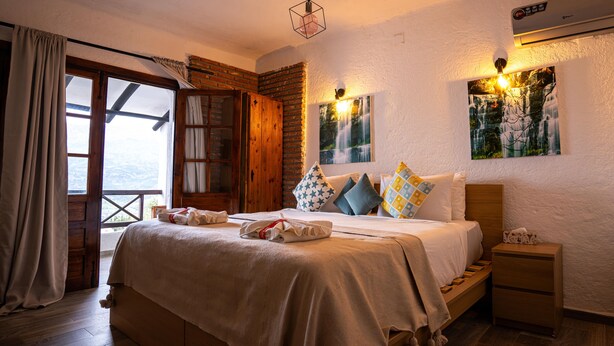 Ein gemütliches Schlafzimmer mit einem großen Bett, einem Nachttisch aus Holz und Blick ins Freie durch ein Fenster.
