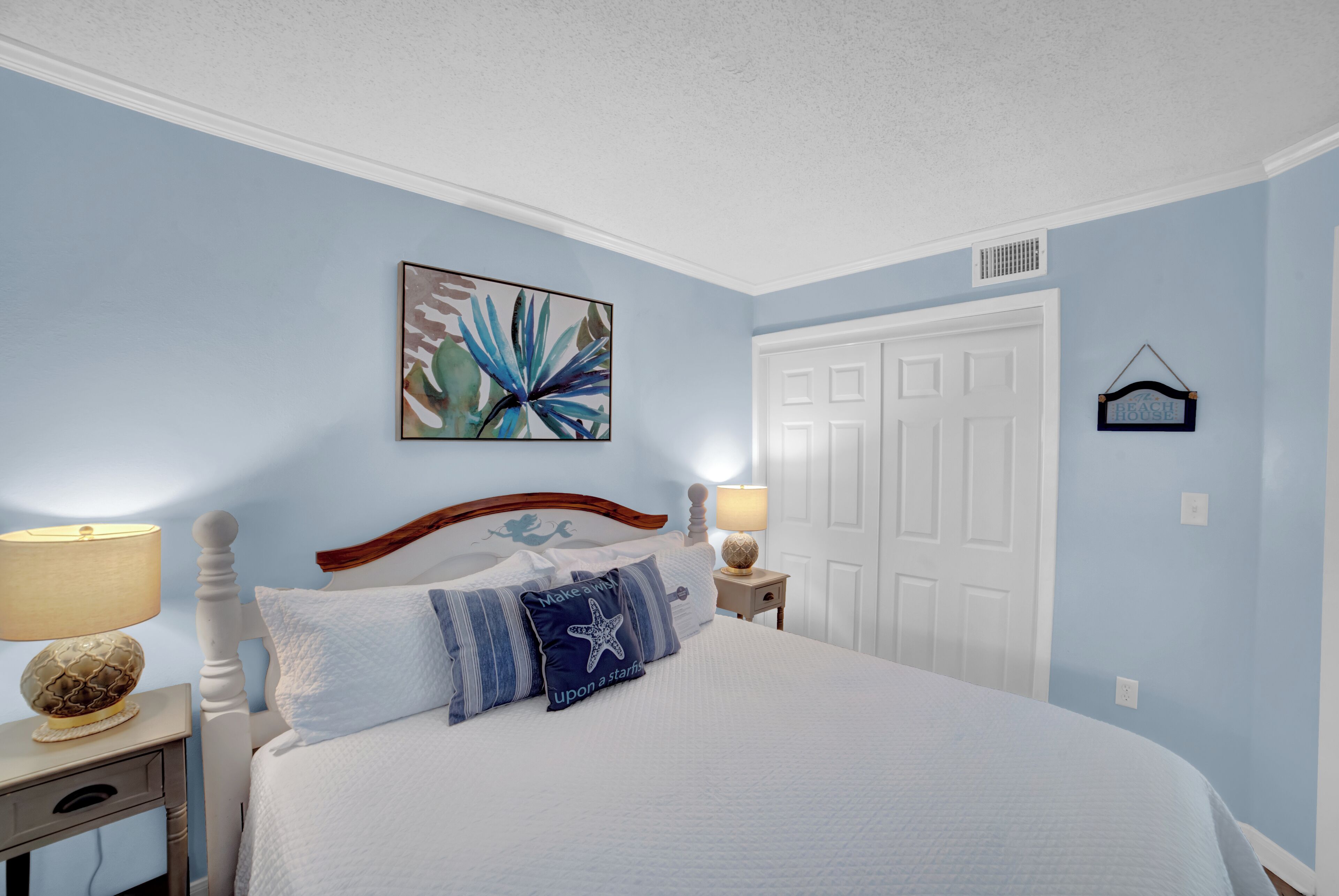 A bedroom with a bed, two bedside tables, a nightstand, a door, and a wall-mounted artwork.