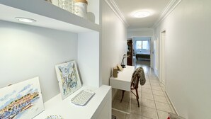 Een gang met een wit bureau, stoel en planken met decoratieve voorwerpen.