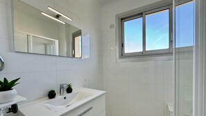 Een moderne badkamer met een witte wastafel, een grote spiegel en een raam.