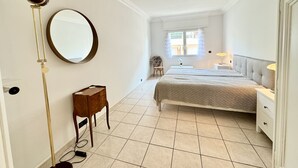 Een slaapkamer met een bed, nachtkastjes, een spiegel, een vloerlamp en een klein houten kastje.