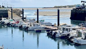 A marina with boats docked, a sandy beach, and a rocky outcrop in the background. - The Cliffs  A Ribeira - Polas (Foz)