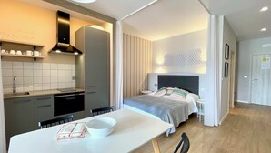 A modern, compact hotel room with a kitchenette, a bed with a headboard, a dining table, and a whiteboard on the wall. - The Cliffs  A Ribeira - Polas (Foz)