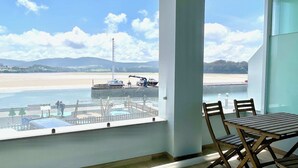 Un balcon avec vue sur une plage et un quai où sont amarrés des bateaux.