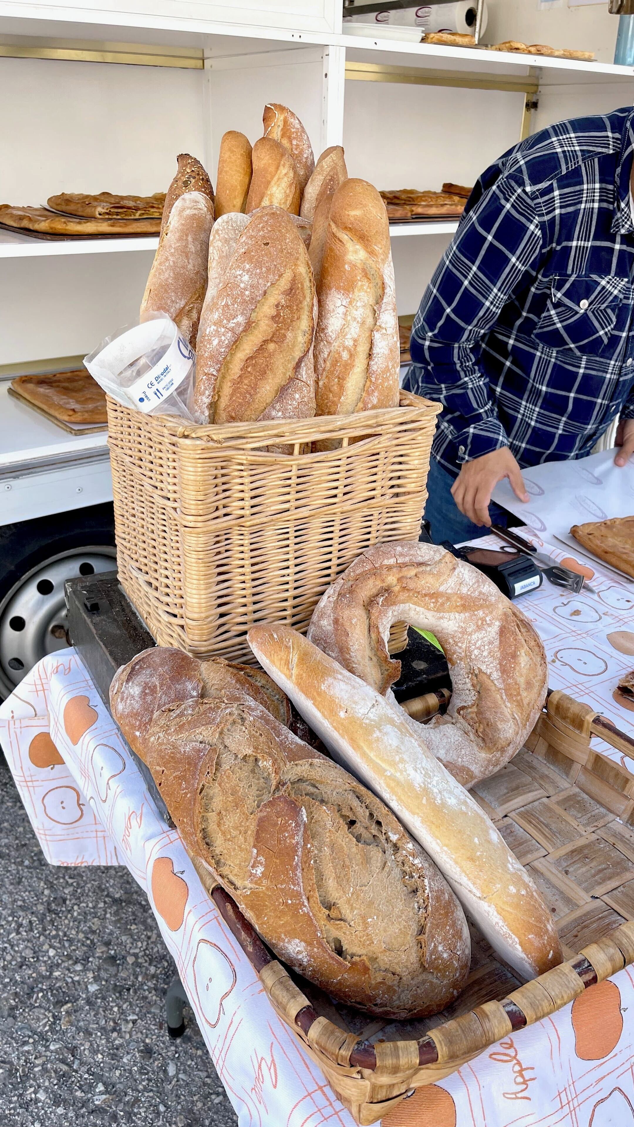 A variety of breads displayed on a table with a basket of baguettes and a loaf of bread on a cutting board.