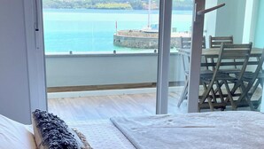 A bedroom with a bed, a view of a body of water, and a balcony with a chair. - The Cliffs A Ribeira - Peizas (Foz)