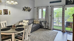 A dining area with a round table, chairs, and a chandelier. There is a sofa with patterned cushions, a rug, and a window with curtains. A sign on the wall reads "LOON MOUNTAIN." - Kitchen, AC, deck, mountain view, pool, ski shuttle. LB307 by LRS (Lincoln)