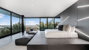 A modern bedroom with a large bed, a seating area, and a city view through large windows.