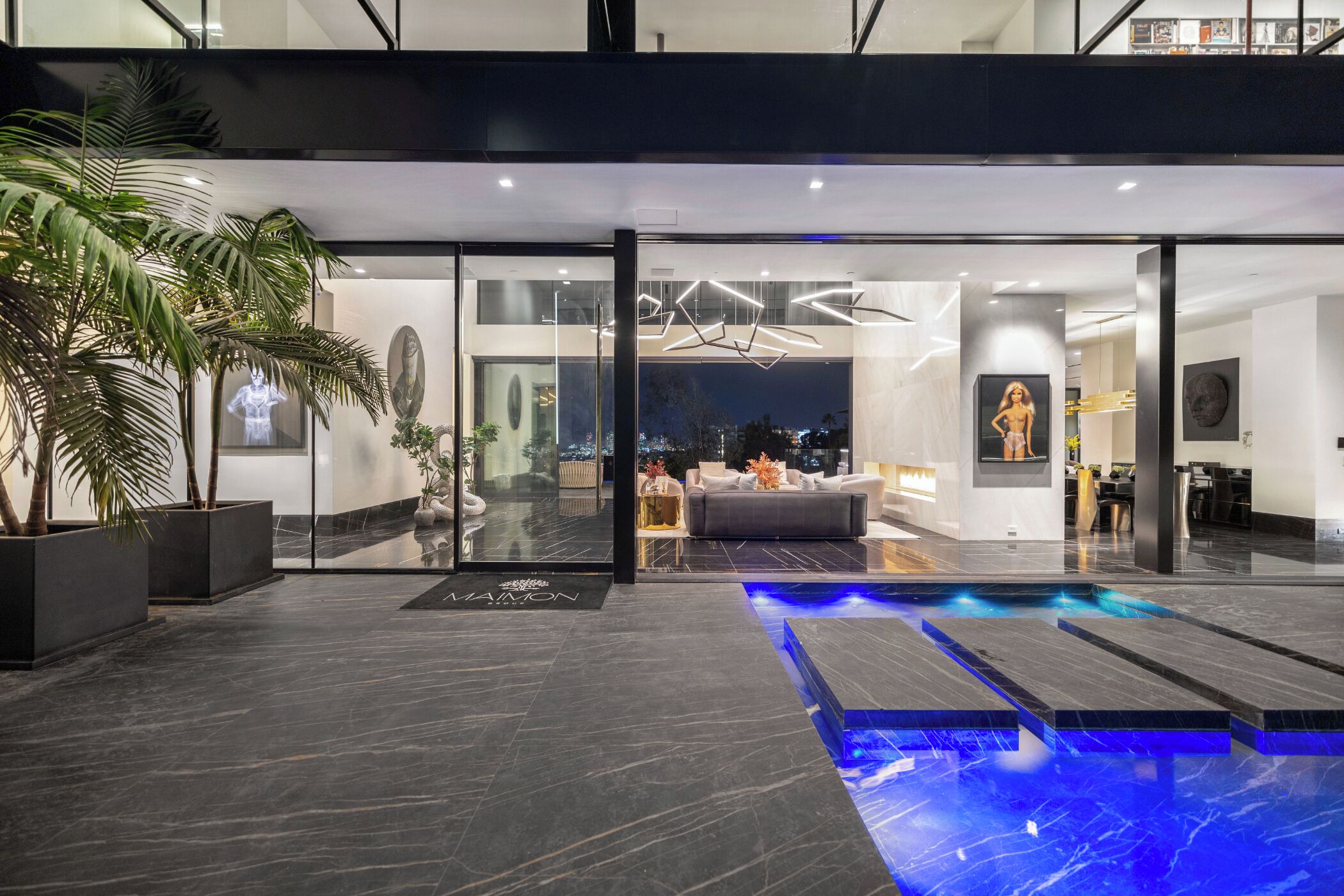 A modern hotel interior with a glass entrance, a pool area, and a living room with a sofa and decorative items.