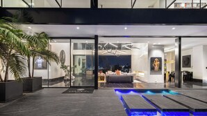 A modern hotel interior with a glass entrance, a pool area, and a living room with a sofa and decorative items.