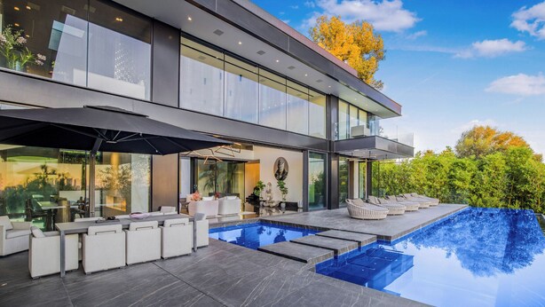 A modern house with a large glass facade, a swimming pool, and outdoor seating.