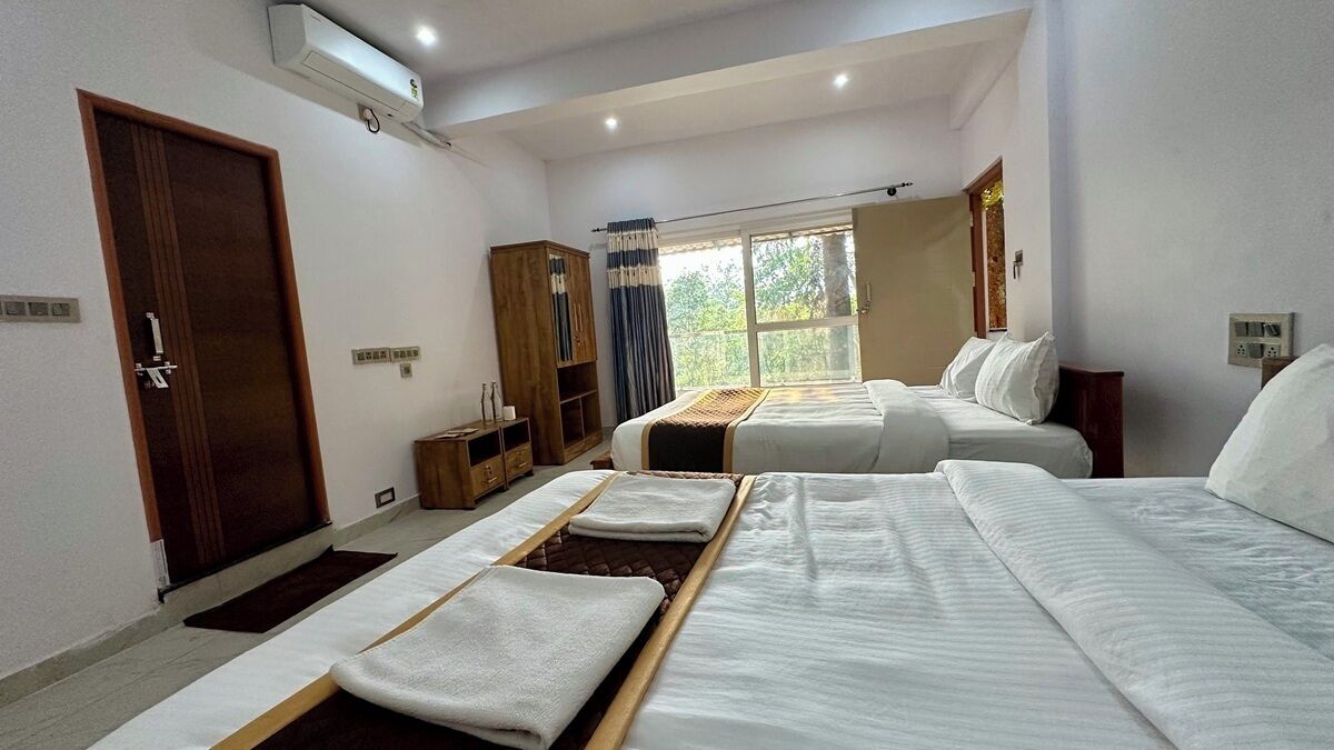 A hotel room with two beds, a wardrobe, a window with curtains, and a door.