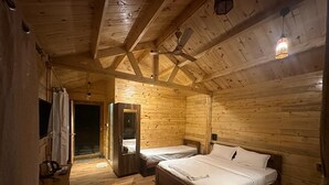 Habitación de cabaña de madera con una cama grande, dos camas más pequeñas, un escritorio y un espejo.