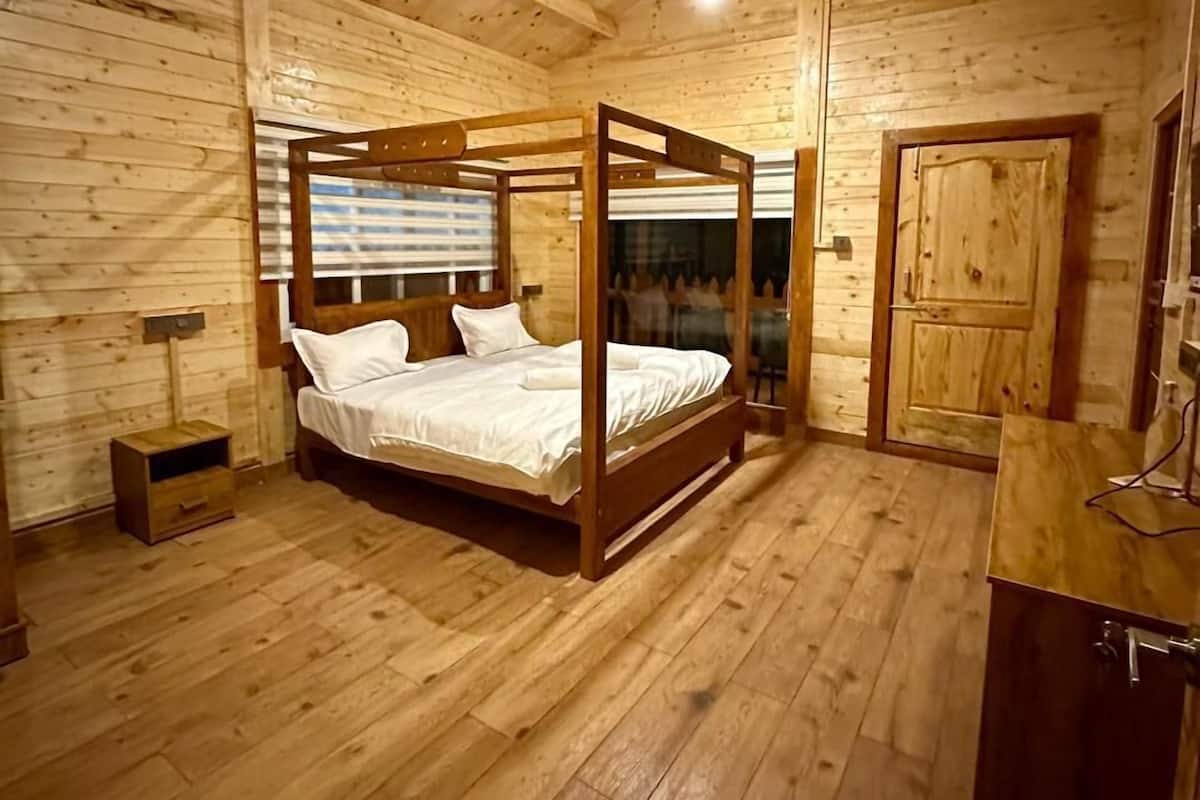 A wooden cabin bedroom with a four-poster bed, a small bedside table, a wardrobe, and a door.