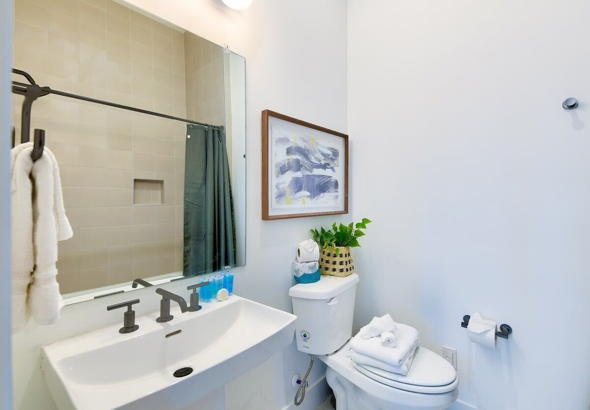 A bathroom with a sink, mirror, toilet, and a framed picture on the wall.