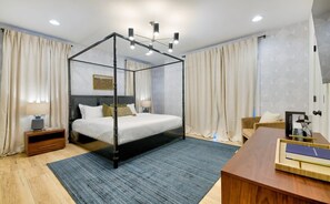 A modern bedroom with a four-poster bed, a wooden desk, and a chair.